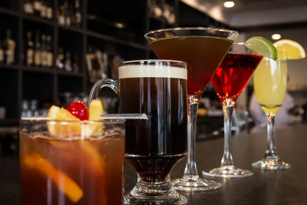 Five assorted drinks on a dark, reflective bar top.
