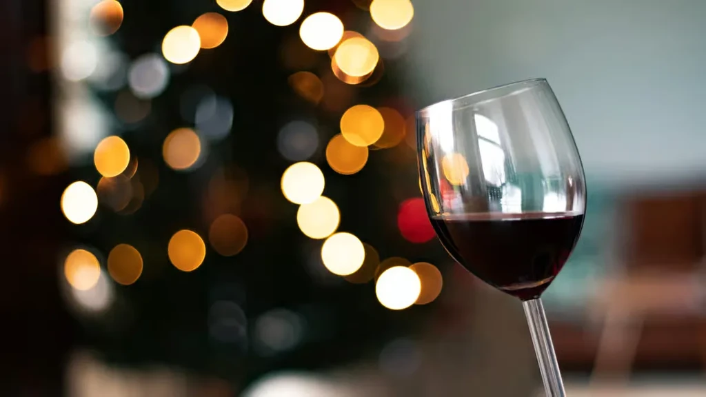 Clear red wine glass against a dark, blurred background with warm lights.