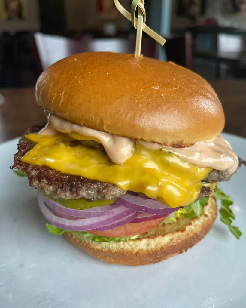 Close-up of a burger with melted cheese, beef patty, and fresh vegetables.