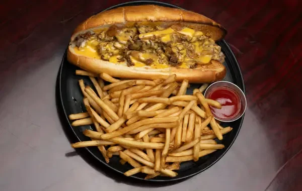 Close-up of a cheesesteak, french fries, and ketchup on a black plate.