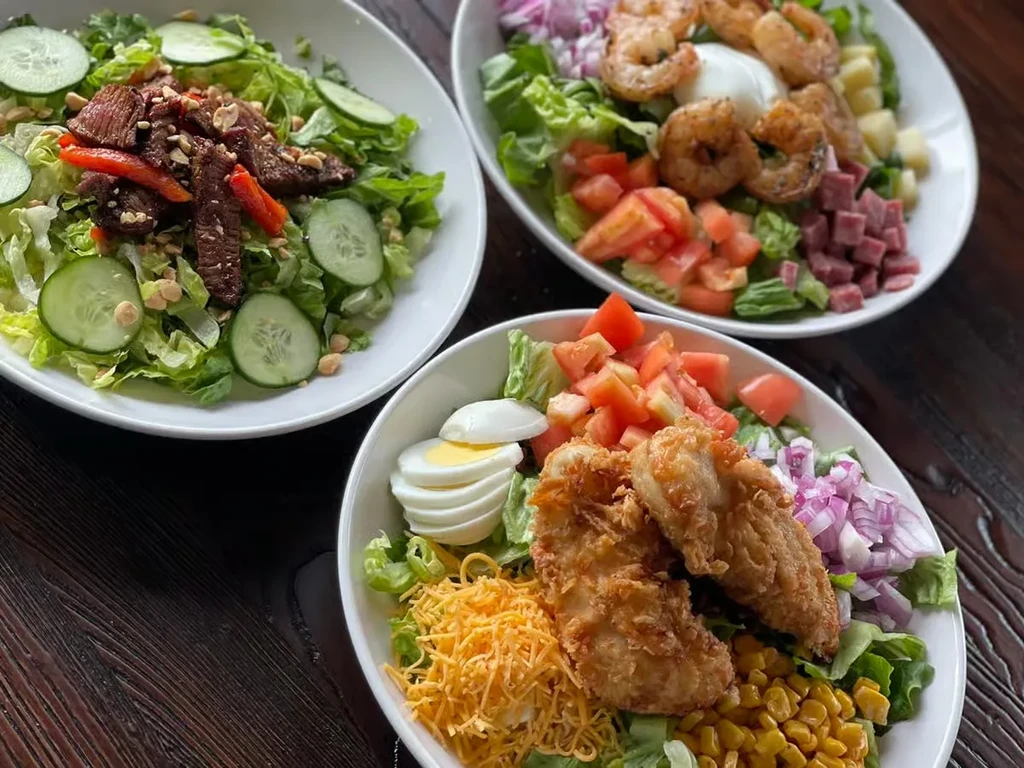 Three colorful salad bowls with beef, shrimp, and chicken.