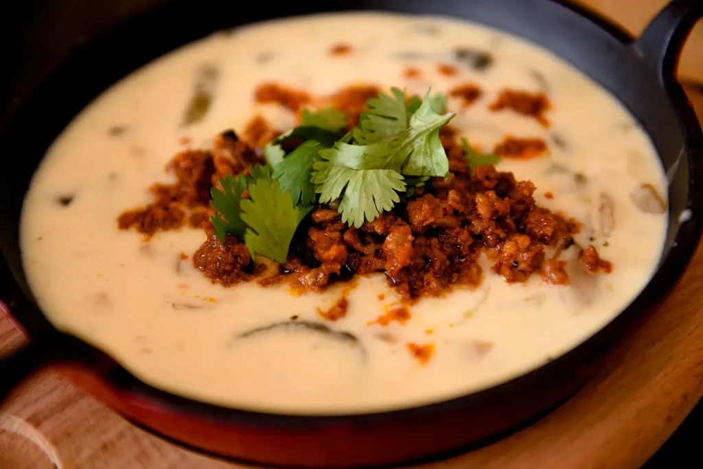 Creamy yellow dip, crumbled meat, and cilantro in a dark pan.