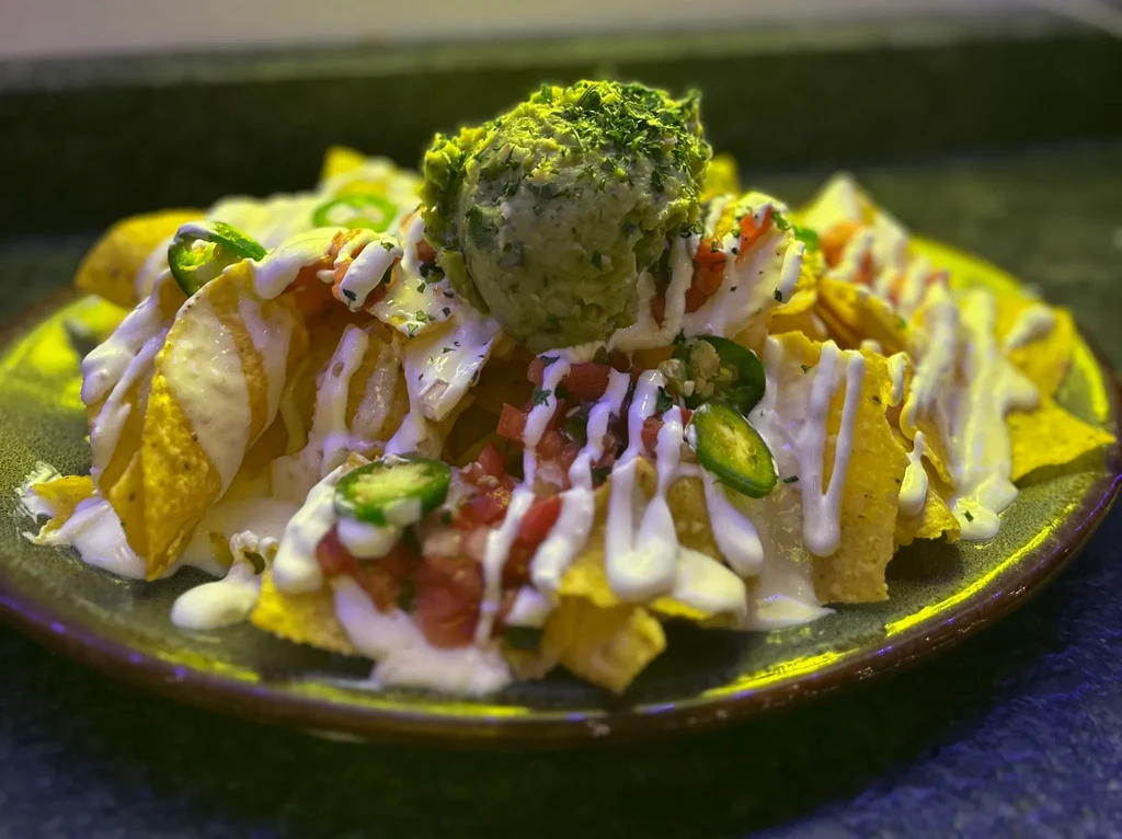 Piled high nachos with guacamole, creamy sauce, diced tomatoes, and jalapeños.
