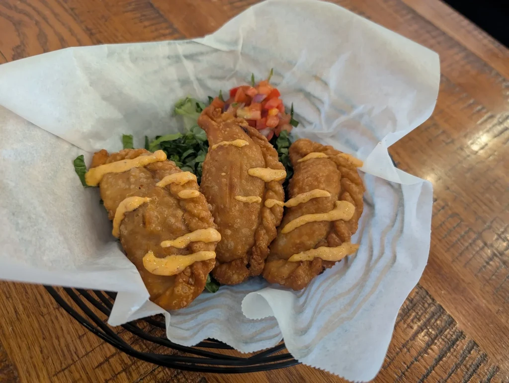 Three golden empanadas with orange sauce, pico de gallo, lettuce.