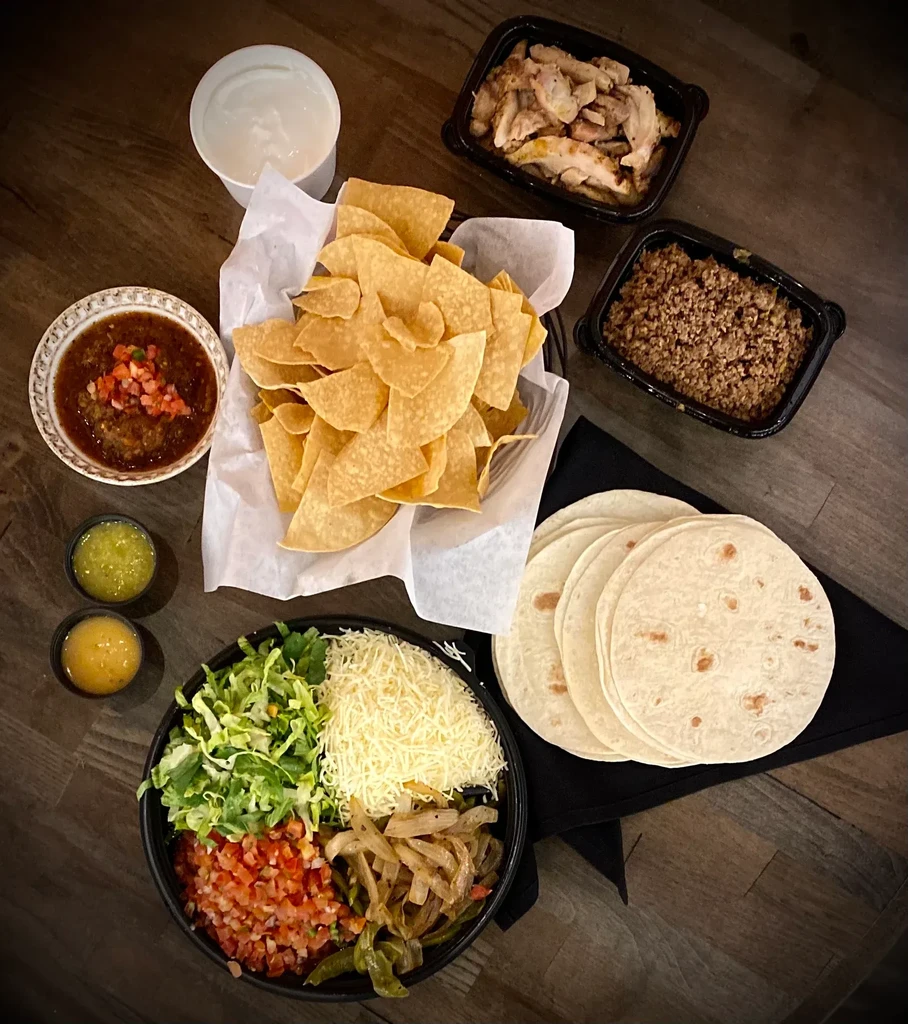 Mexican food spread with chips, meats, tortillas, salsa, and assorted toppings.