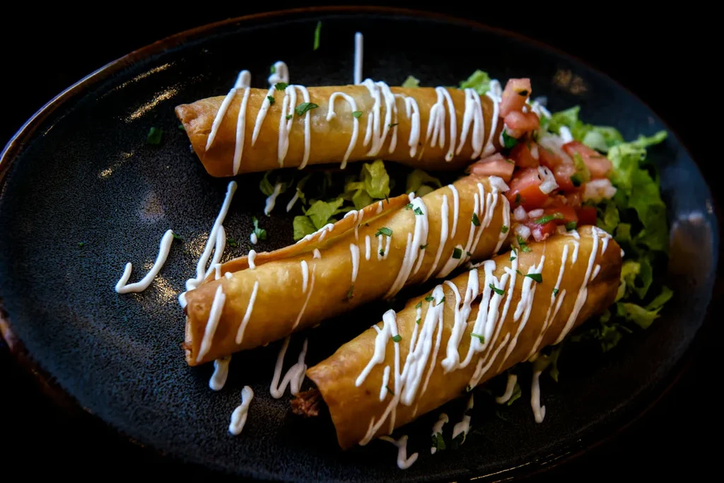 Three crispy rolled tacos with cream, herbs, lettuce, and pico de gallo.