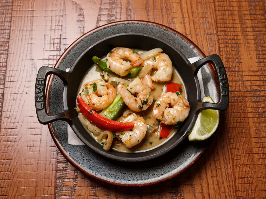 Plump shrimp scampi with peppers, lime, and sauce in a skillet.