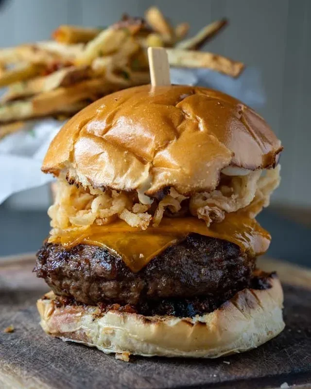 Gourmet beef burger with melted cheese, crispy onions, and fries.