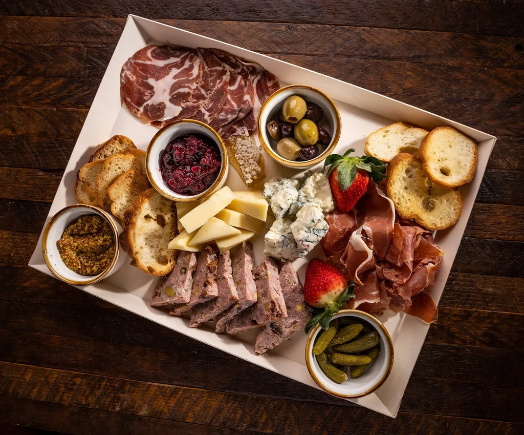 Rectangular charcuterie board with various meats, cheeses, olives, and fruit.