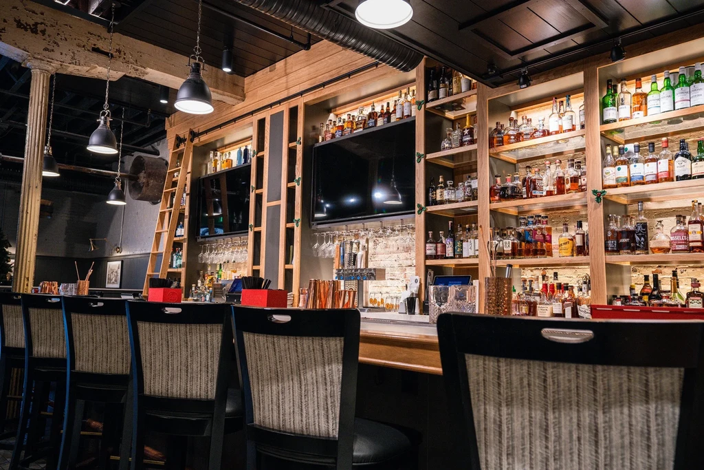 Interior of a well-stocked bar with shelves of spirits and empty stools.