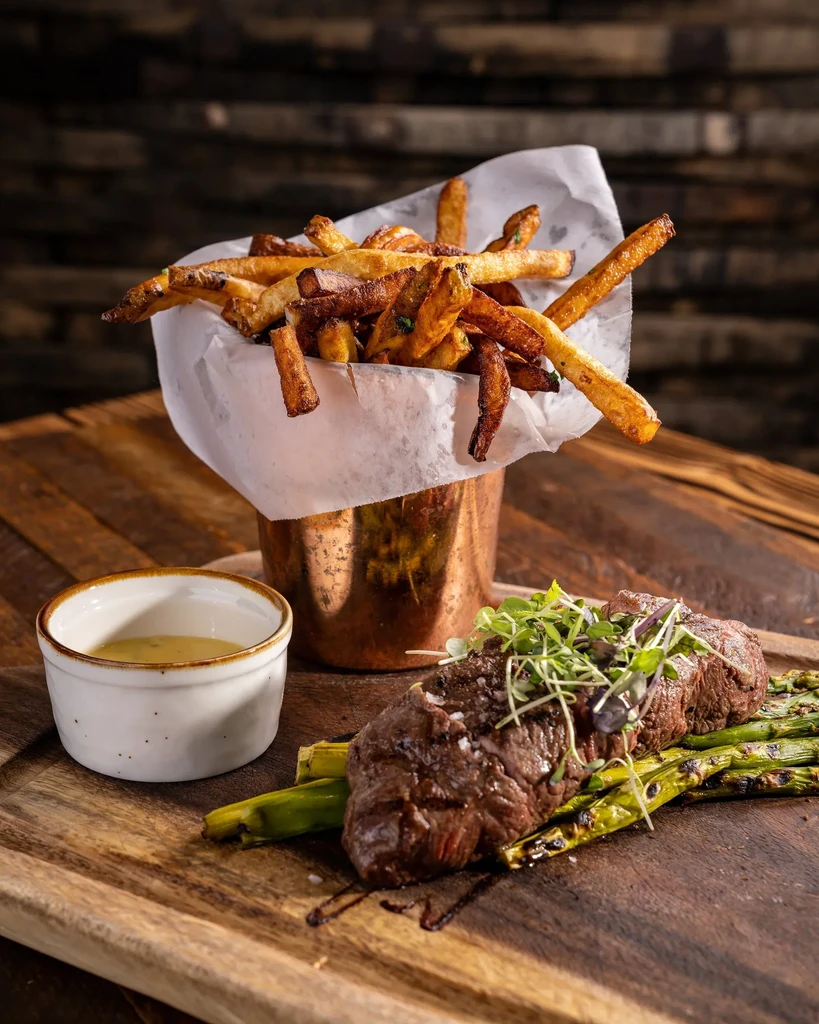 Medium-rare steak, grilled asparagus, dipping sauce, and crispy fries.