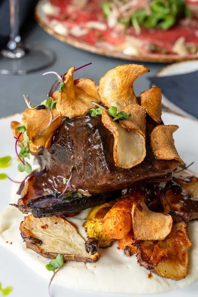 Braised meat with crispy chips, microgreens, purée, and roasted vegetables.