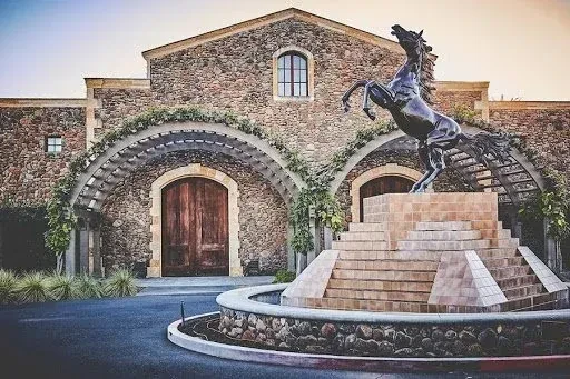 Grand stone building with arched green pergolas and a rearing horse statue.