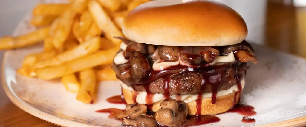 Gourmet burger with melted cheese, sautéed mushrooms, sauce, and french fries.
