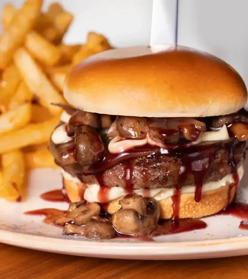 Double-patty burger with brioche bun, mushrooms, red sauce, and fries.