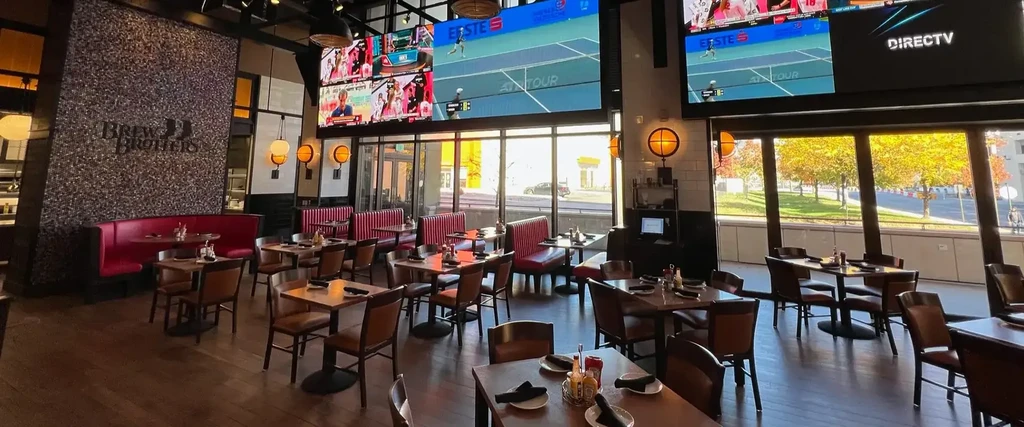 Empty Brew Brothers restaurant interior with red booths, sports screens, autumn view.