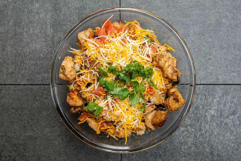 Overhead view: glass bowl with grilled chicken, cheese, tomatoes, cilantro.