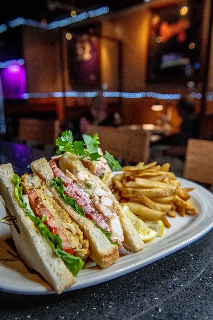Club sandwich, fries, lemon, and parsley on a white oval plate.