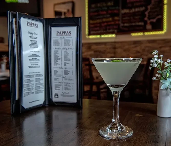 Martini cocktail with mint and open Pappas menu on a dark table.