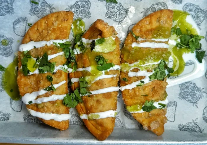 Three golden-brown fried crescent pastries with white and green sauces, cilantro.