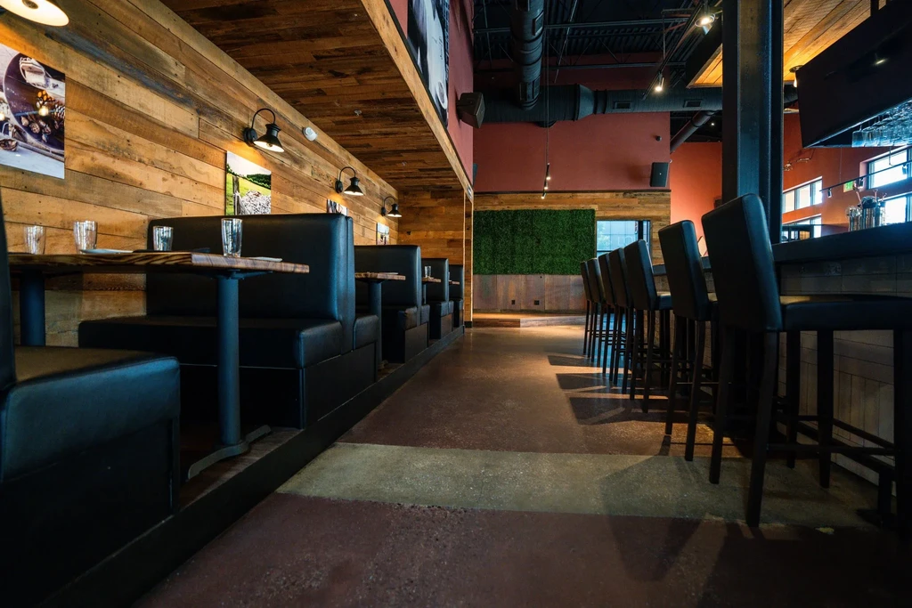 Modern restaurant interior with rustic booths, industrial bar, and foliage wall.
