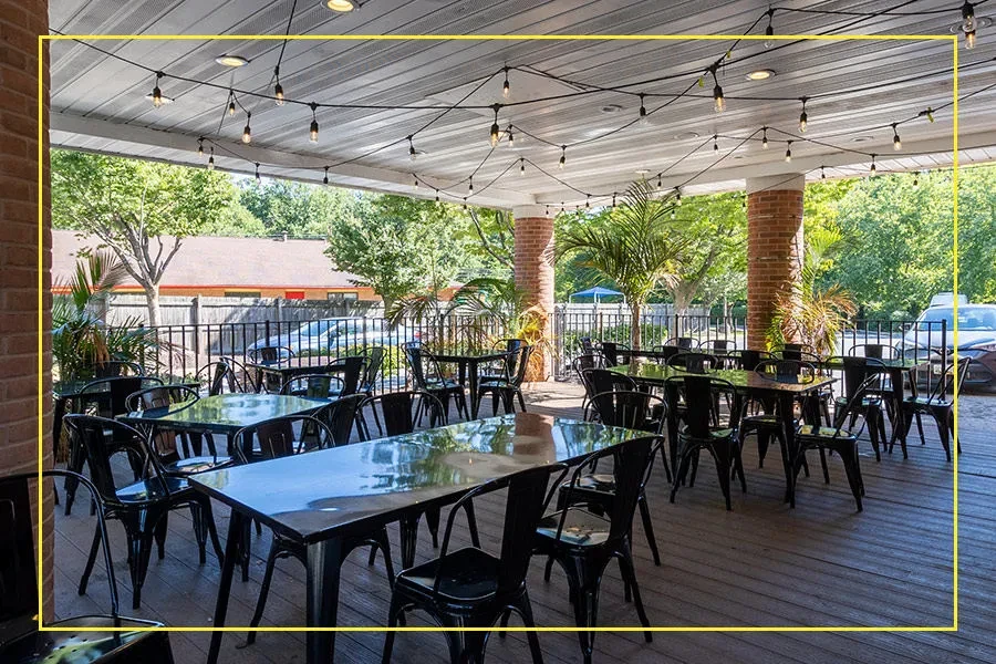 Outdoor restaurant patio with black tables, string lights, and palm trees.