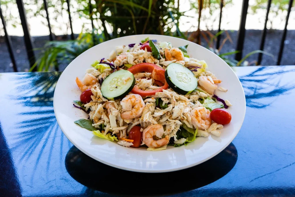 Seafood salad with shrimp, crab, tomatoes, and cucumber on a blue table.