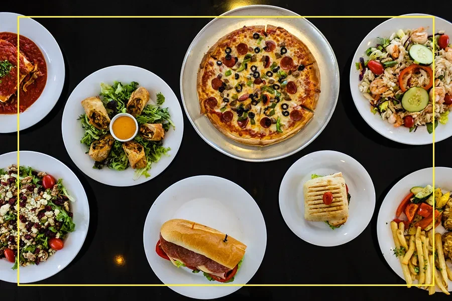 Flat lay photo of eight distinct food plates on a dark surface.