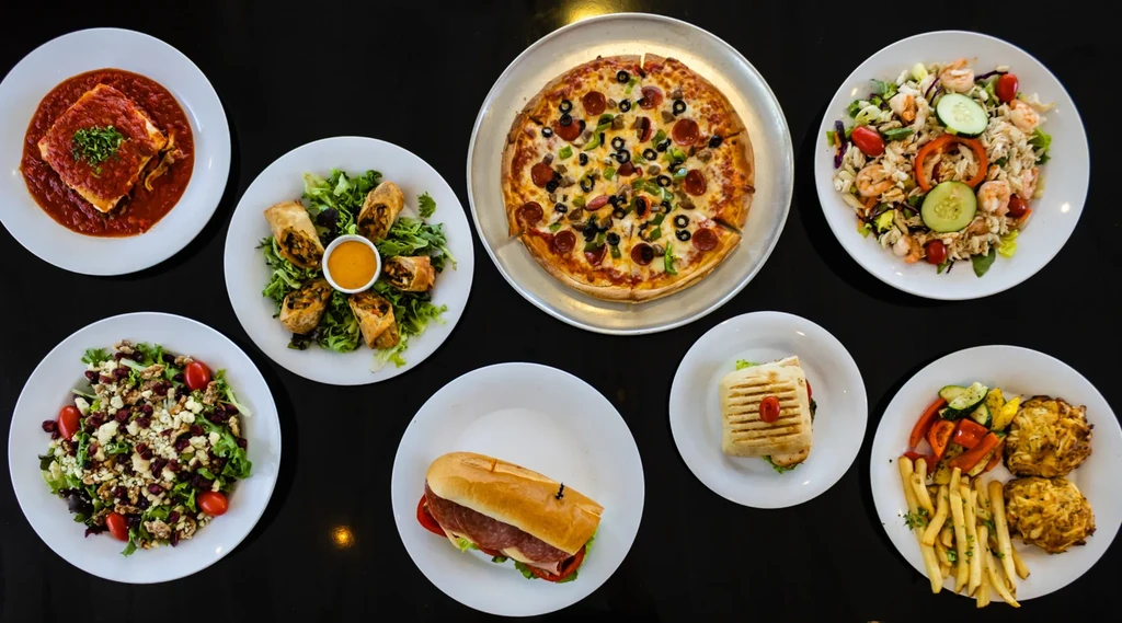Eight diverse food dishes meticulously arranged on a dark surface.