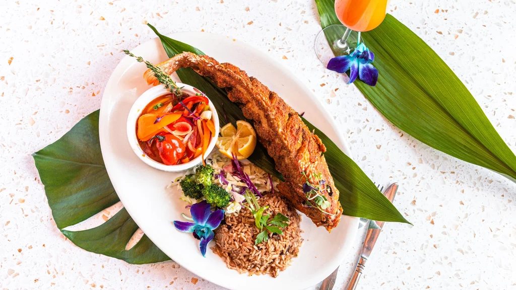 Overhead view of whole fried fish meal with rice, vegetables, and orchids.