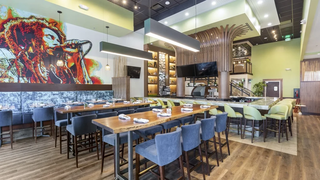 Modern restaurant with Bob Marley mural, communal tables, bar, and tree structure.