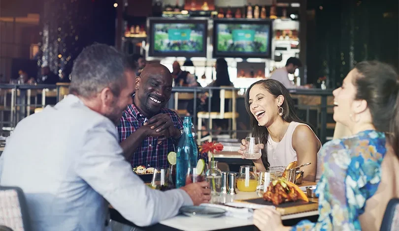 Four smiling people enjoying drinks and appetizers at a restaurant.