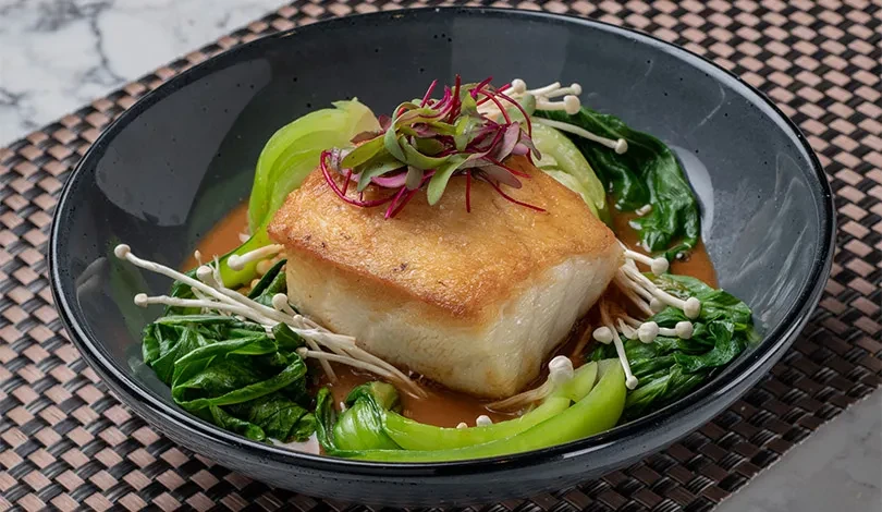 Seared white fish or tofu, bok choy, enoki, microgreens in a ceramic bowl.