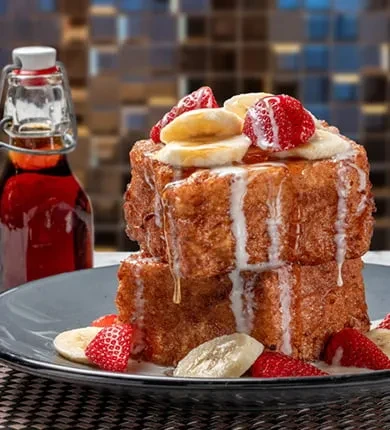 French toast stack with strawberries, bananas, glaze, and maple syrup.