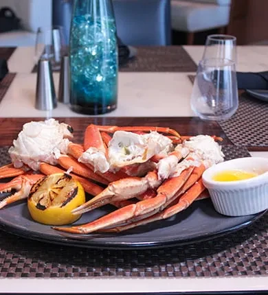 Cracked crab legs, grilled lemon, and melted butter on a dark plate.