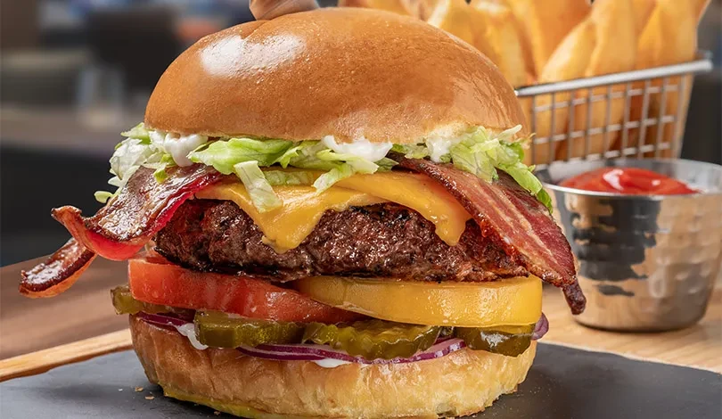 Close-up of a stacked gourmet burger with cheese, bacon, fries, ketchup.