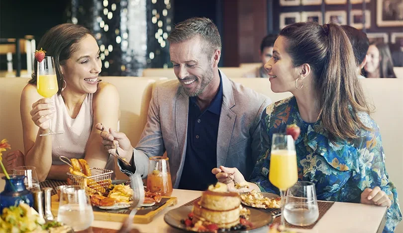 Three smiling diners, two women and a man, in an upscale restaurant.