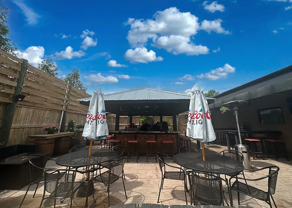 Bright outdoor patio with central bar, tables, and Coors Light umbrellas.