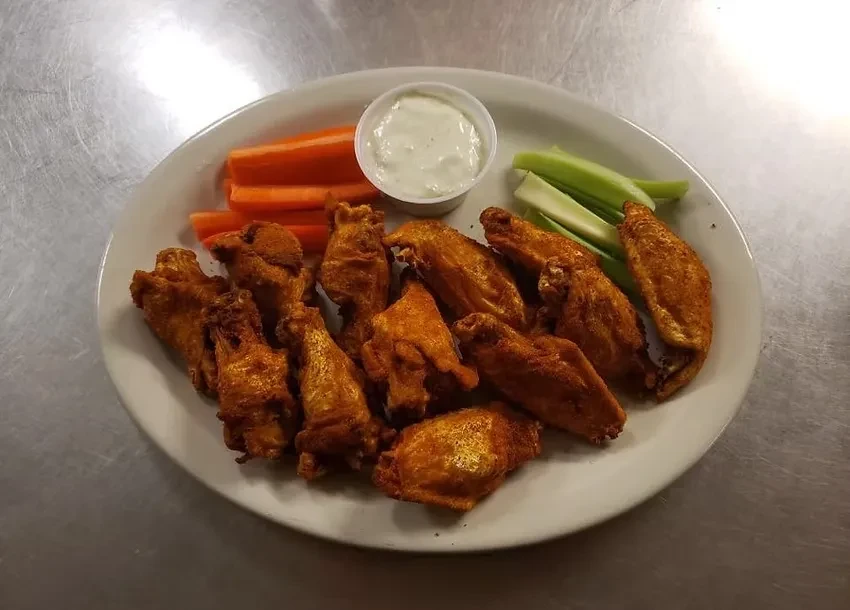 White oval plate of golden-brown buffalo wings, carrots, celery, and dip.