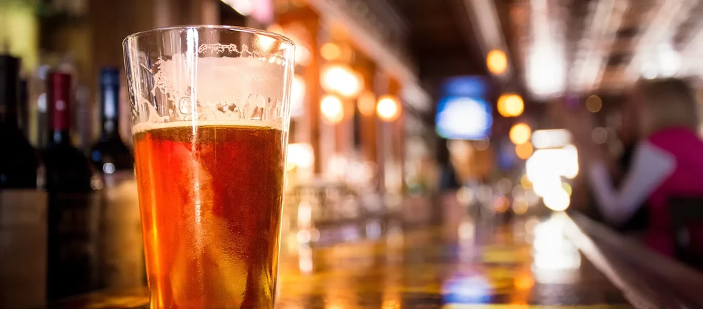 Cold pint glass of amber beer on a bar, blurred background.