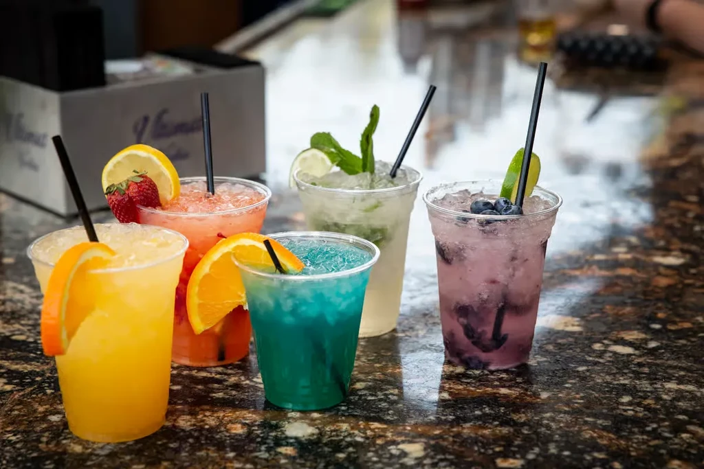 Five vibrant, colorful beverages with ice and garnishes on a bar.