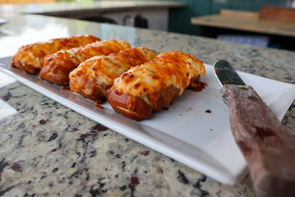 Close-up of cheesy pretzel dogs on a white platter and granite counter.