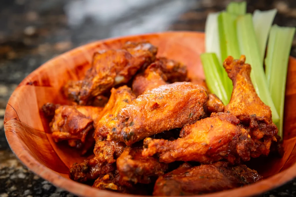 Crispy buffalo chicken wings in a rustic wooden bowl with fresh celery.