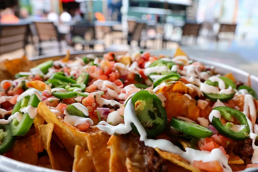 Platter of loaded nachos with ground meat, cheese, tomatoes, and jalapeños.