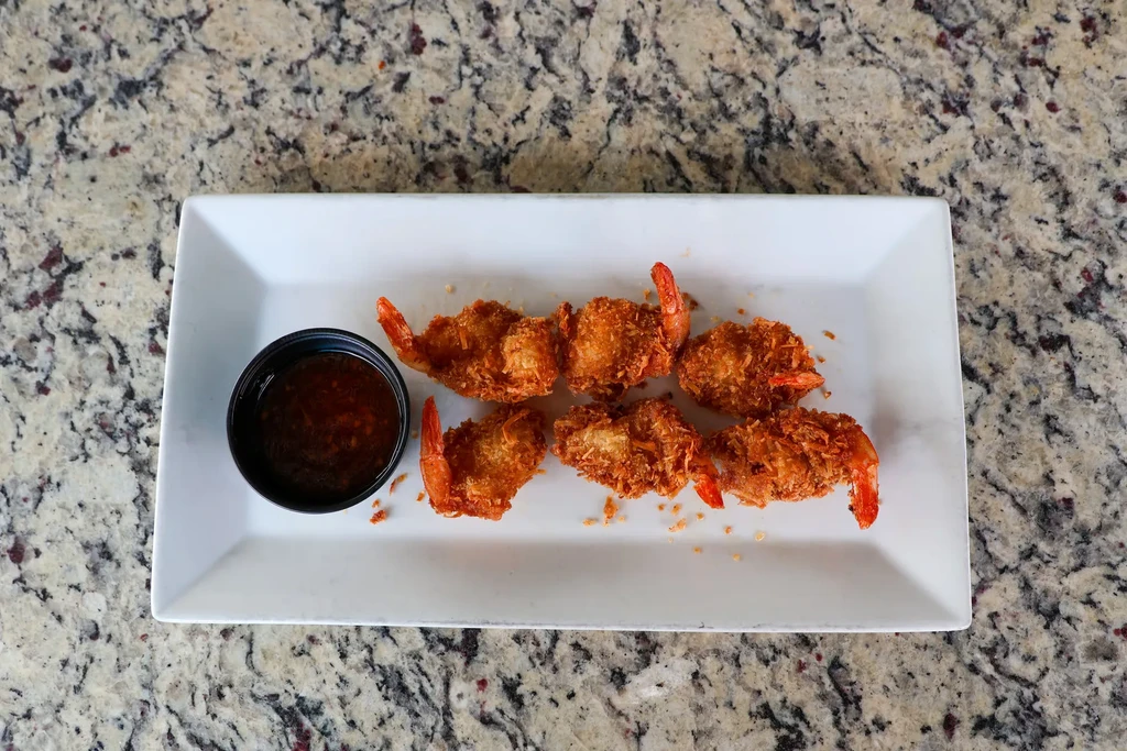 Six golden-brown breaded shrimp, dipping sauce, white plate on granite.