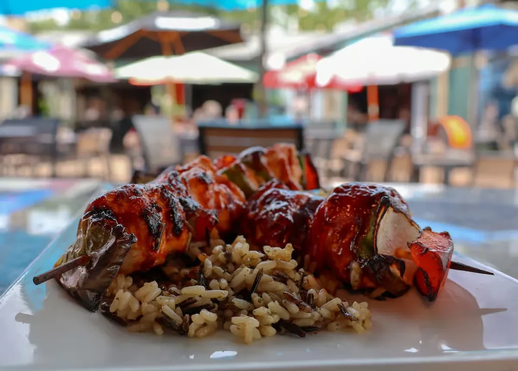 Glazed grilled skewers with wild rice on a plate outdoors.