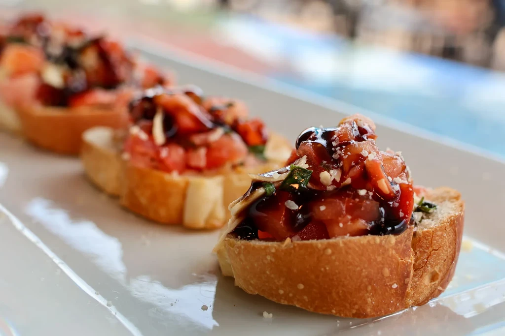 Three bruschetta with diced tomatoes, green herbs, balsamic glaze.