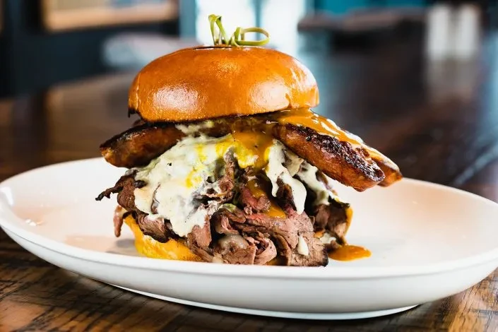 Towering roast beef sandwich with melted cheese, orange sauce, and sausage.