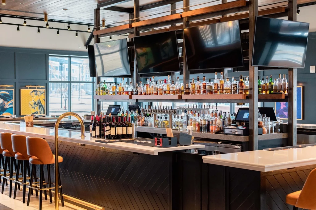 Empty modern bar with illuminated liquor shelves and orange stools.