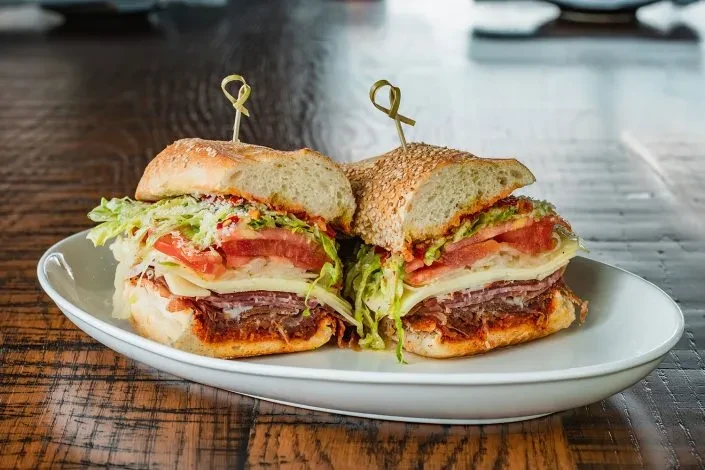 Half-cut hoagie sandwich with meat, cheese, lettuce, tomatoes on a wooden table.